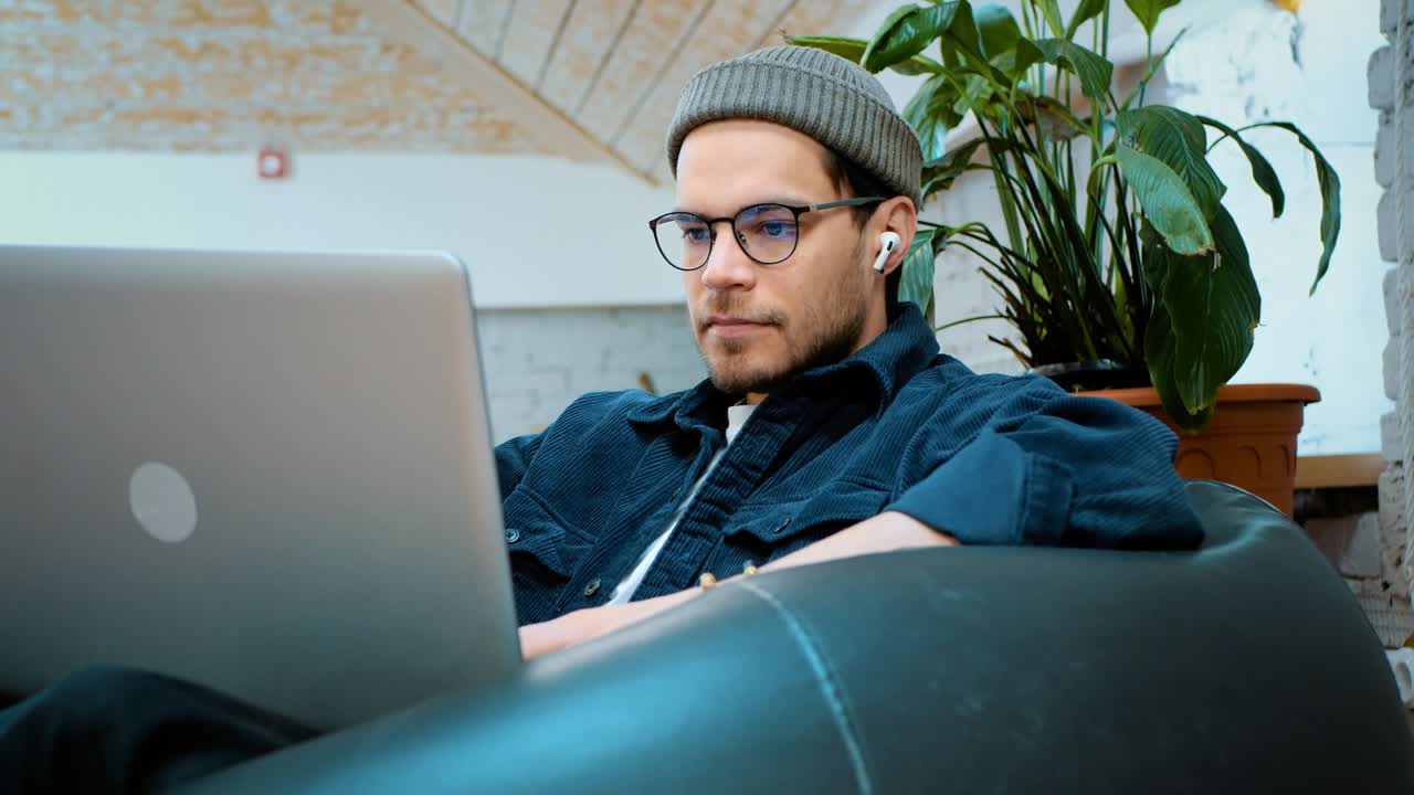 A young guy sits in an open space on an easy chair. Works on a laptop..