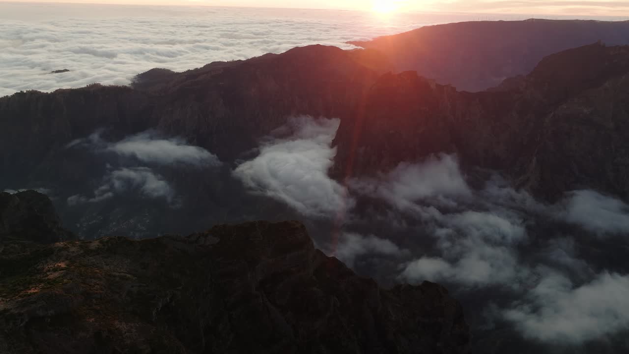 Dramatic sunset light spills over mountain peaks and drifting clouds above a lush valley in Madeira, Portugal.