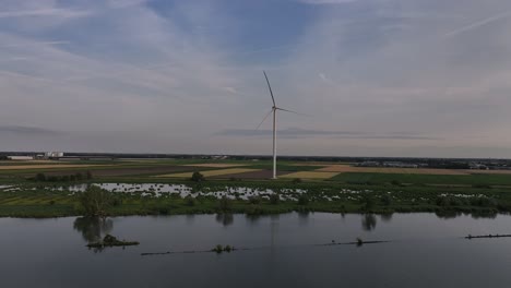 a wind turbine by a serene lake at sunset with fields in the background, aerial view