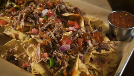 nacho pile of corn tortilla chips slathered with queso cheese sauce pulled pork and pico de gallo salsa, close up slider 4k