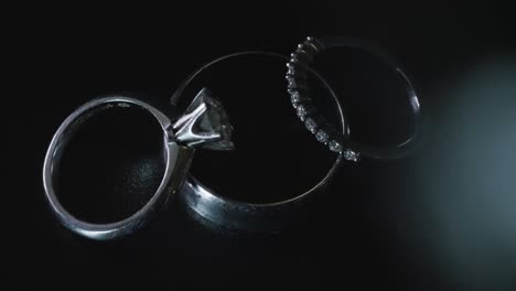 Anillos-De-Boda-De-Diamantes-Plateados-Sobre-Superficie-Negra.