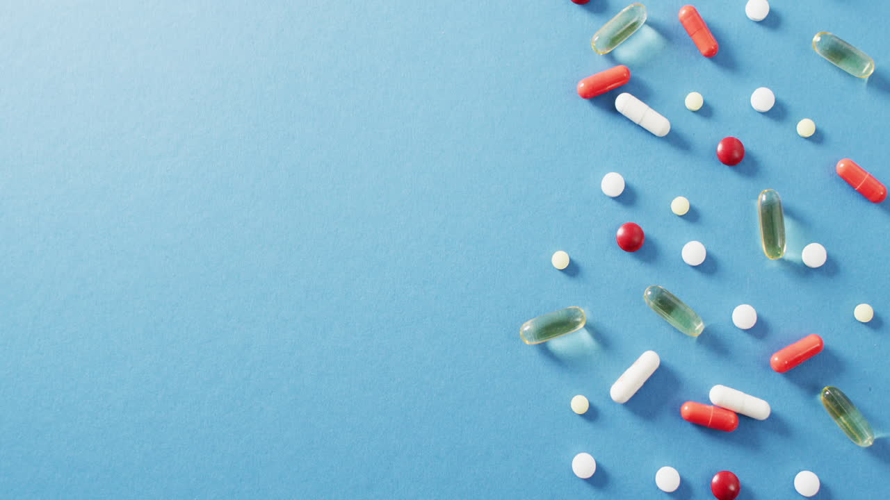Video of a variety of pills and capsules on blue background with copy space