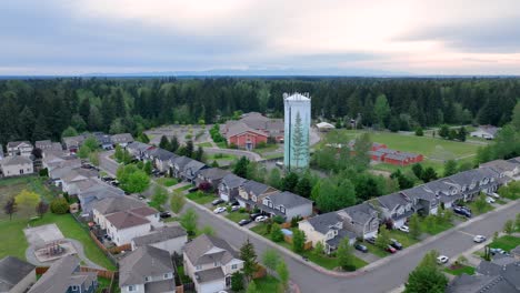 Toma-Aérea-En-órbita-Alrededor-De-Una-Torre-De-Agua-Suburbana-Con-Un-Vecindario-En-Primer-Plano