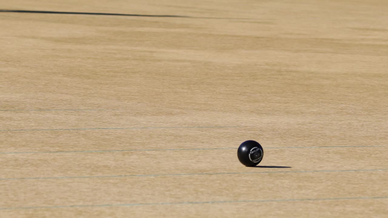 A player skillfully rolls a ball on a sunny lawn bowls green, capturing the sport's precision and focus