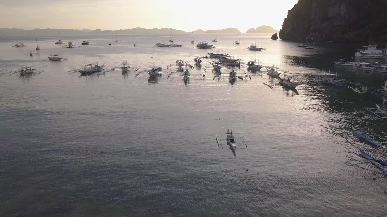 필리핀 팔라완 엘 니도에 있는 코롱 코롱 해변에서 일몰 동안 베이에 정박한 아우트리거 반카 방카 보트의 4k 공중 드론 샷