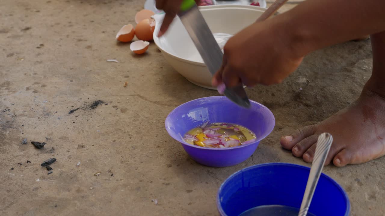 preparación de tortilla para acompañar con dumpling banko, mujer africana corta cebolla y la agrega al huevo batido en un plato, ghana