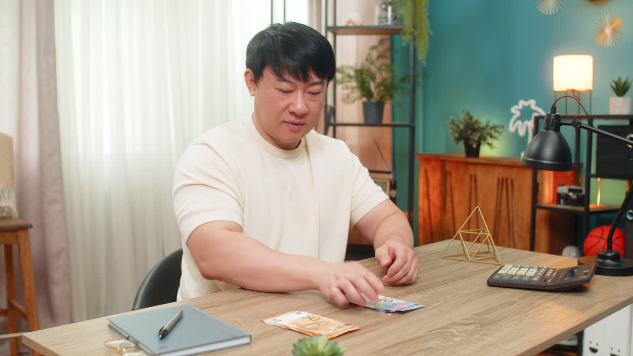 Asian man counting euro cash carefully setting some aside satisfied with smart money management