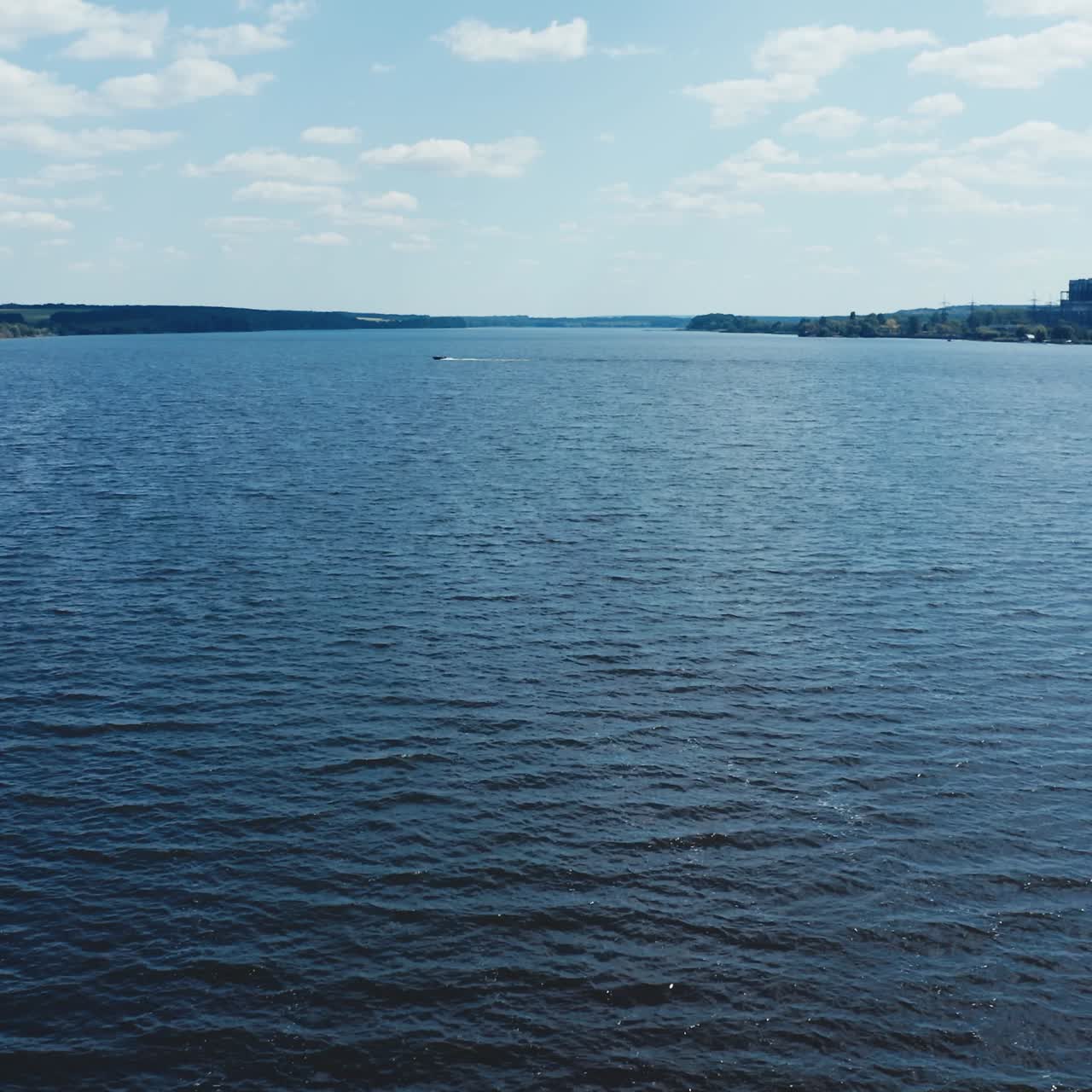 Quick motion camera over the blue river. Natural water background. Industrial factory near the river. Beautiful lake under the blue sky.