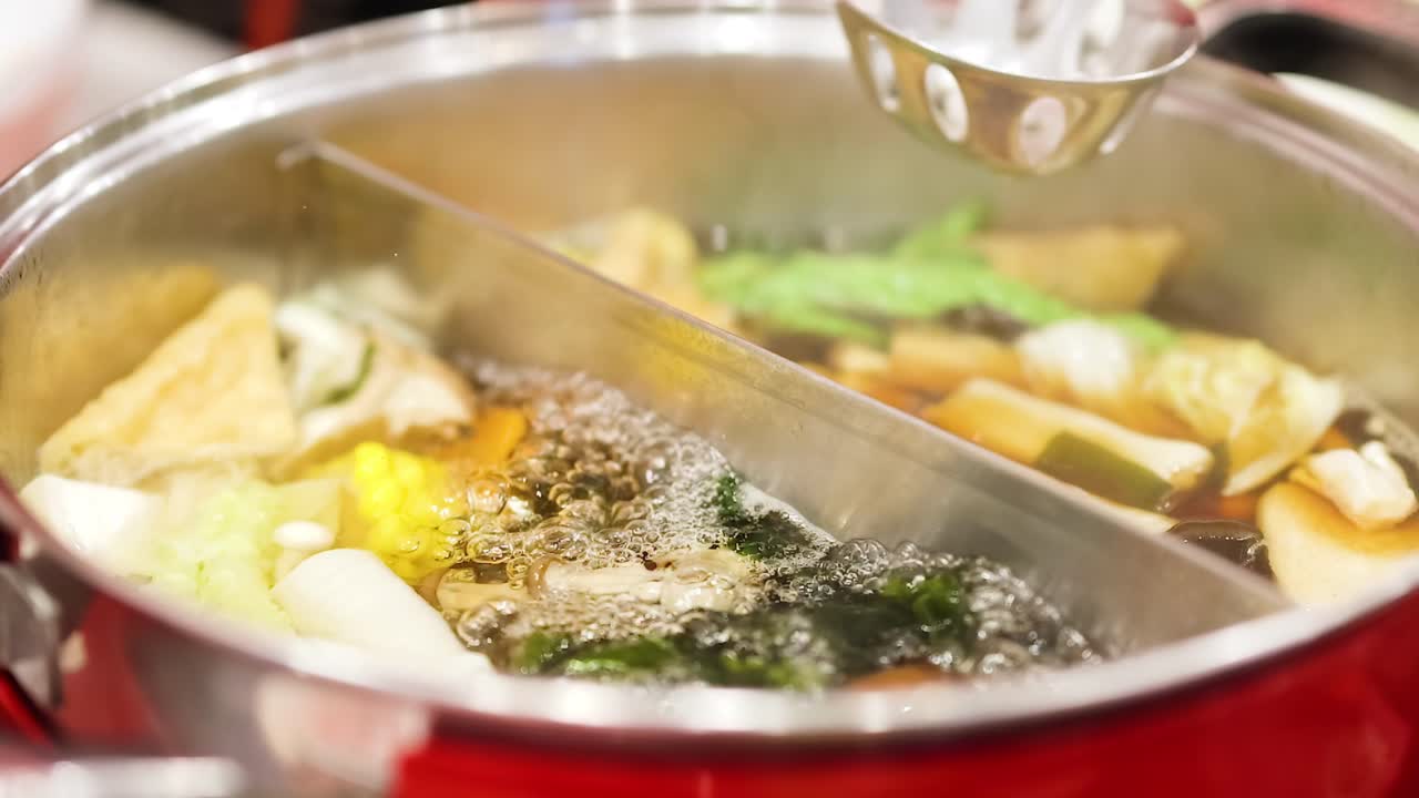 Close-up view of a hotpot with bubbling broth and fresh vegetables cooking.