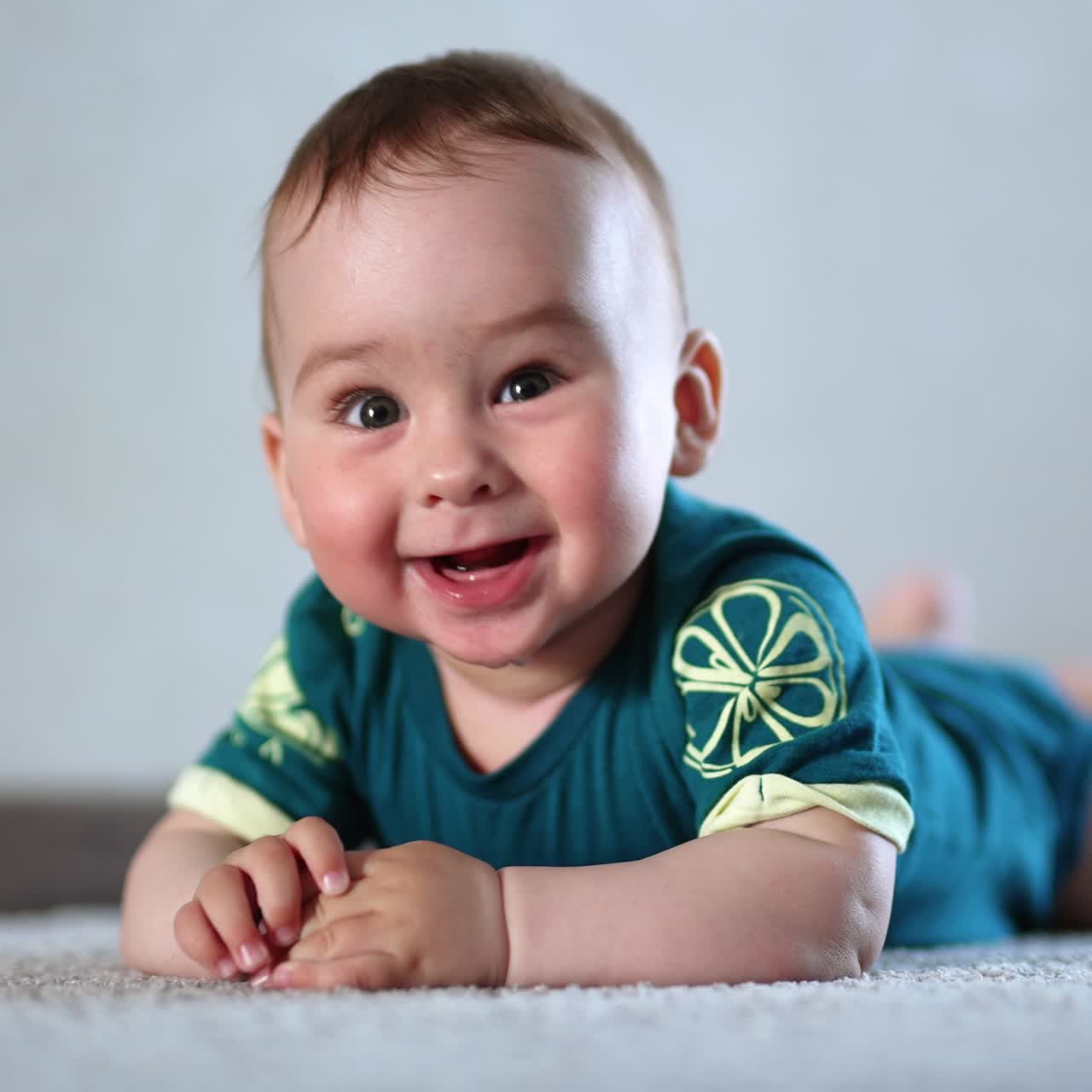 Beautiful Caucasian healthy child lies on the carpet on his belly. Lovely kid looking into camera with his eyes wide-open. Close up