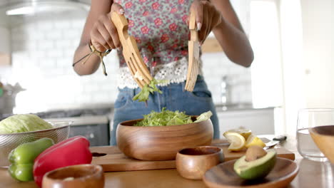 using wooden utensils, woman preparing fresh salad in kitchen
