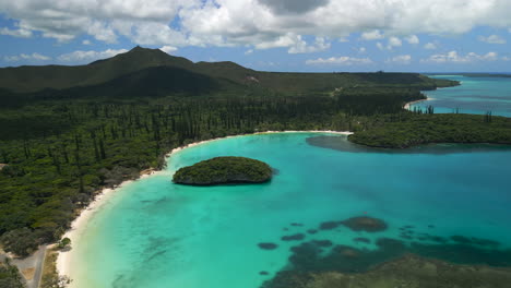 het witte zandstrand van de kanumera-baai, het denneneiland en een zicht op de heilige rots in de lagune - oplopende luchtfoto