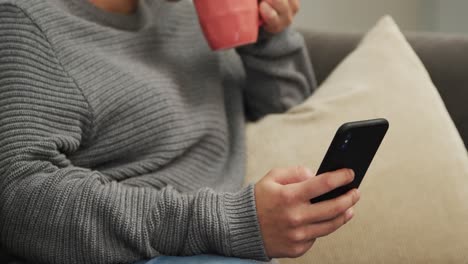 Frau-Benutzt-Smartphone-Und-Trinkt-Einen-Kaffee-Im-Wohnzimmer