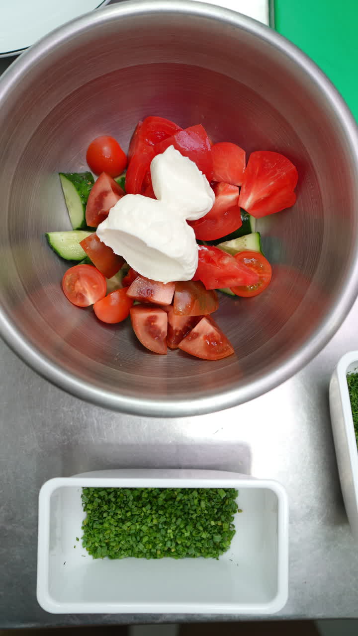 Vertical footage Chopped tomatoes and cucumbers are placed in a metal bowl, followed by mayonnaise, onions, and a sprinkle of fresh dill, creating a vibrant and appetizing salad