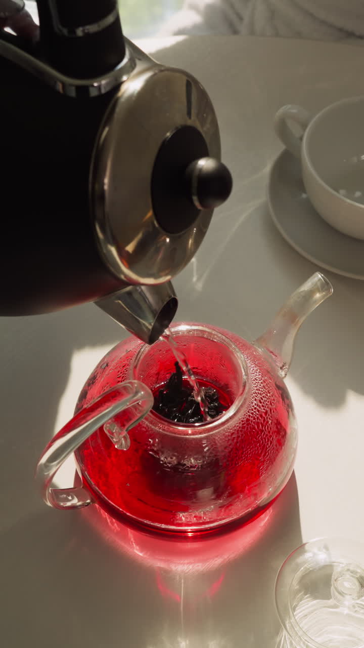 Process of crafting wholesome beverage. Half-full teapot of brewed tea continues filling with water from kettle. Man makes natural fruit tea