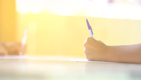 hand holding pen writing paper on table on bright daytime of sunlight