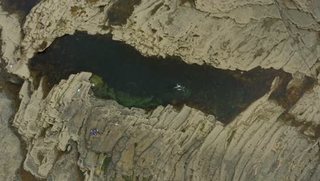 cinematic aerial top-down shot of swimmers enjoying a natural pool, slow motion