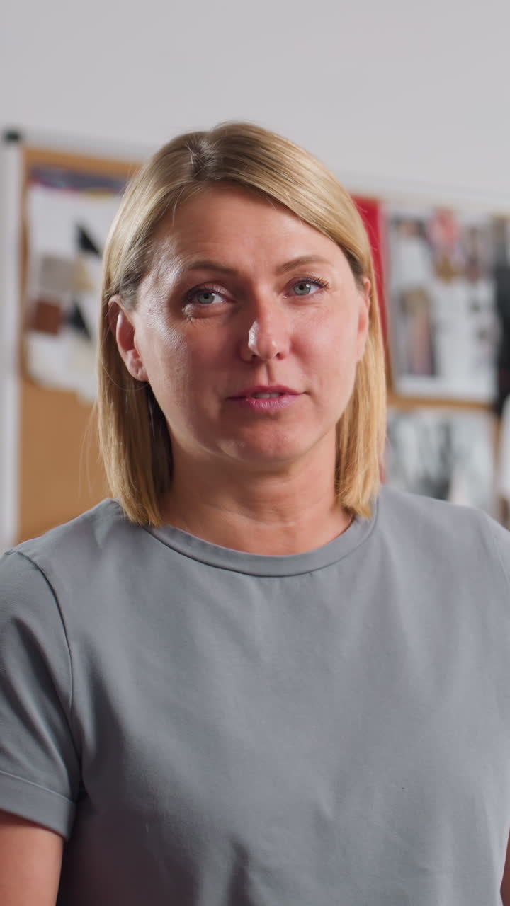 Playful needlewoman lifting black scissors pretending to cut material while smiling joyfully, standing in bright sewing workspace with creative boards and colorful textiles in background