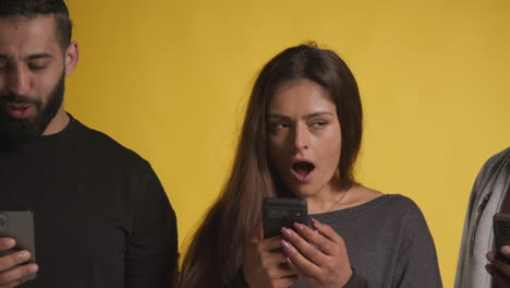 fotografía de estudio de un grupo de amigos con teléfonos móviles celebrando la ganancia de dinero contra un fondo amarillo