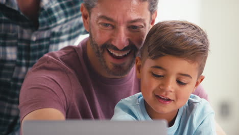 same sex family with two dads and son at home in kitchen using laptop