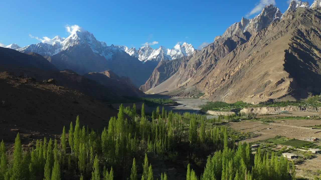 Drone shot of Tupopdan Peak, Passu Cones in Hunza Pakistan, snow covered mountain peaks with steep cliffs, starting in the valley on trees then tilting up to reveal mountains