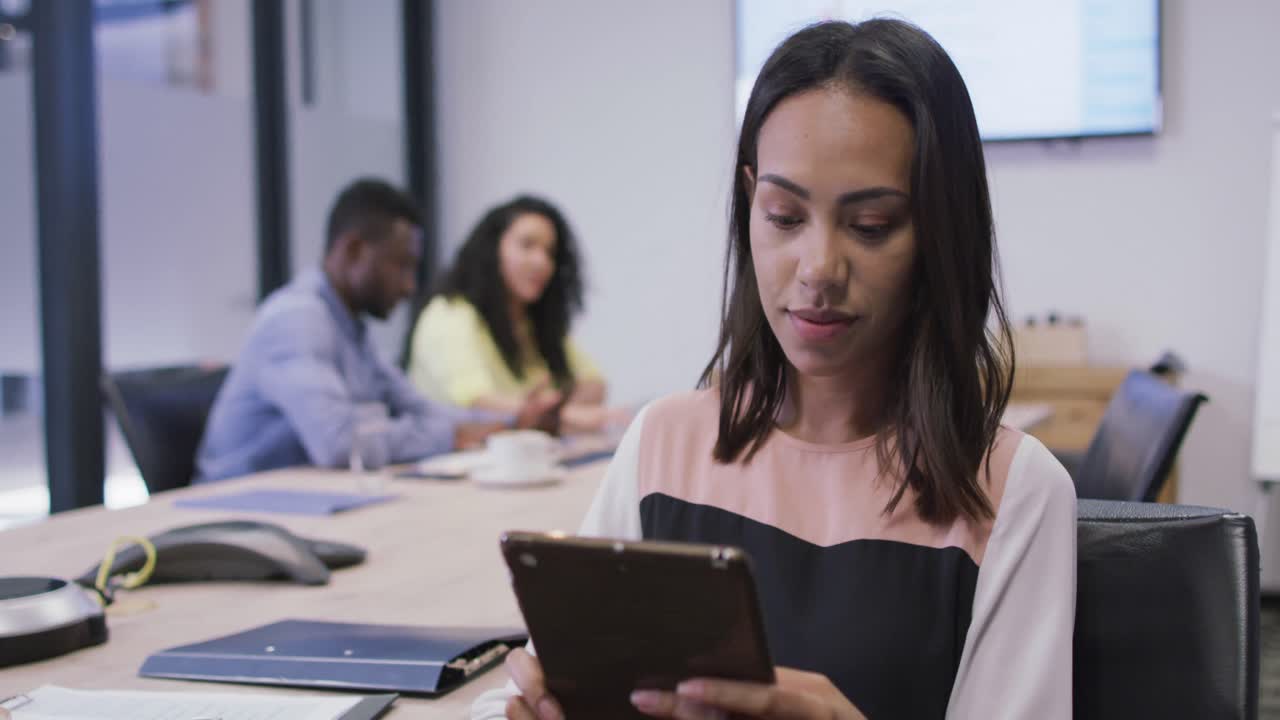 retrato de una mujer de negocios biracial sonriente usando una tableta mirando a la cámara en una oficina moderna