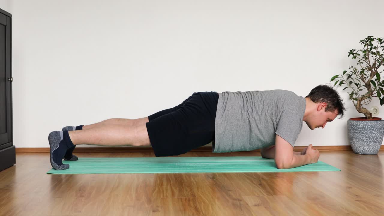 young man doing her workout at home in the living room - plank exercise