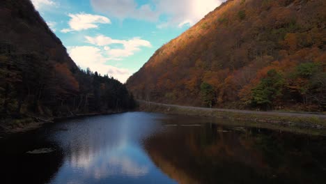 stunning low drone footage over a small pond in a deep autumnal, colorful mountain valley