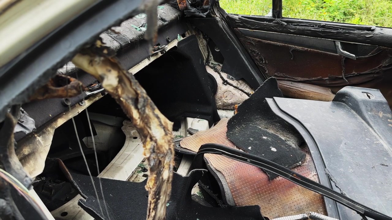 Tracking shot through the back seat of a burned car showing a charred interior damaged upholstery and exposed metal