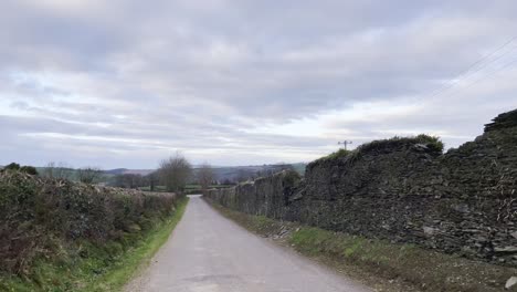 static footage of a rural road in ireland on a cloudy afternoon with stonewall on sides