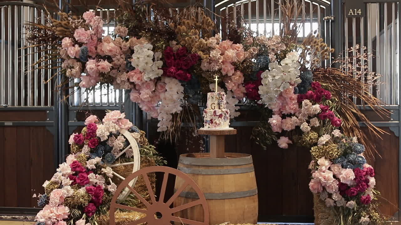 Beautiful decorations with pastel colored flowers and dried leaf details placed in the background for multi-level wedding cake presentation
