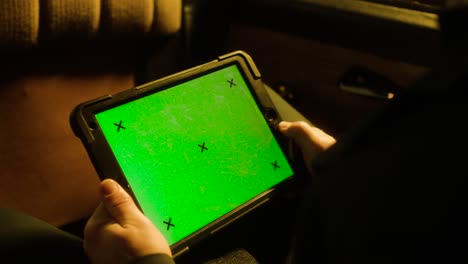 person holding a tablet with a green screen in a dark room