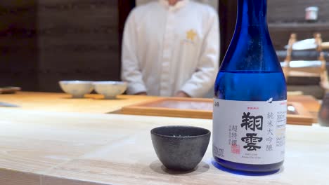 chef prepares sushi with sake bottle visible