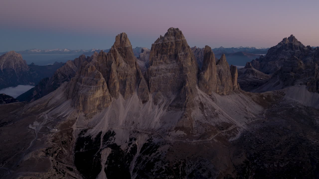 Vista aerea cinematografica delle Dolomiti italiane all'alba, aspre cime rocciose sopra rigogliose colline alpine e chalet sparsi, sereno paesaggio naturale di montagna