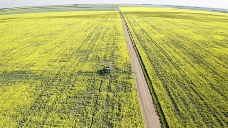 Tractor-Agrícola-Rociando-Los-Hermosos-Y-Vibrantes-Campos-De-Canola-Amarillos-En-Saskatchewan,-Canadá