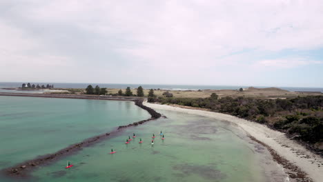 Aerial-backwards-flight-showing-group-of-stand-up-paddlers-paddling-on-private-port-during-sunny-day-with-clouds-in-Australia