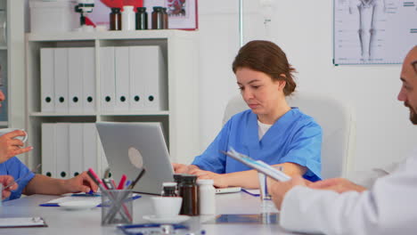 Nurse-writing-on-laptop-during-conference-and-looking-at-camera-smiling