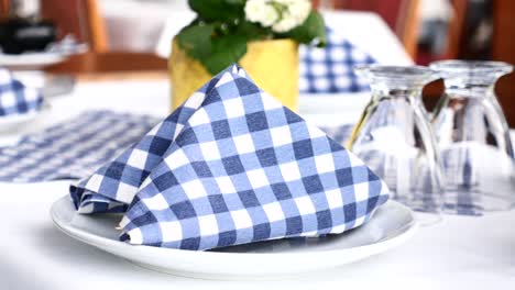 close up of a table setting with a blue and white checkered napkin, a white plate, and a clear glass.