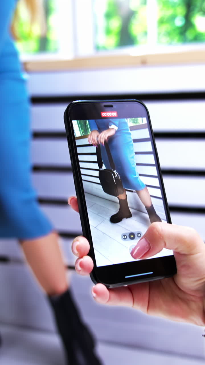 Taking video of a model posing on a smartphone. Brunette woman in blue ...