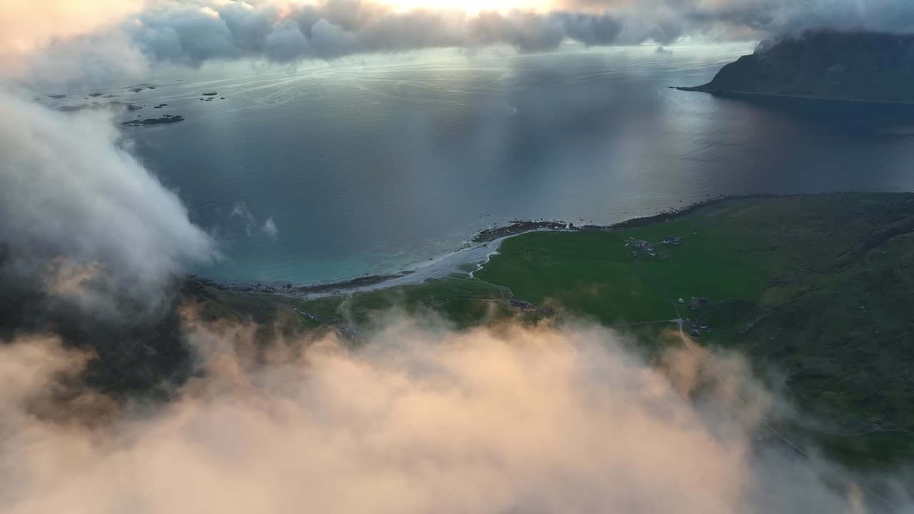 Drone moves forward through illuminated clouds over Utakleiv beach in Lofoten, wrapped in fog and soft midnight light
