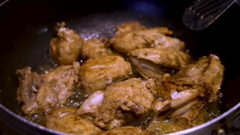 full flavoured chicken pieces sizzling in oil and being stirred by metal slotted spatula