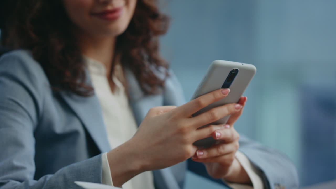 mujer sonriente recibiendo un mensaje en un teléfono inteligente moderno sentada en el lugar de trabajo de cerca.