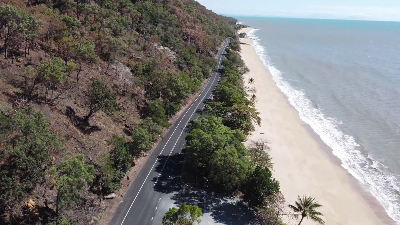 Drone descending over a beautiful sandy beach and a highway near the Pacific Ocean in North Queensland, Australia