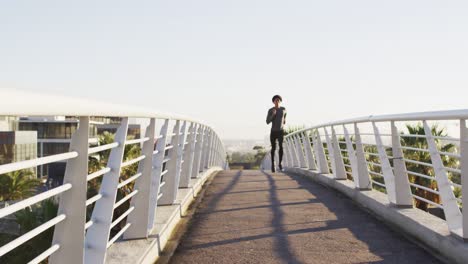 Fit-african-american-man-exercising-outdoors-in-city,-running-on-footbridge