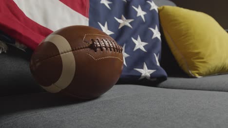 lounge at home of person watching american football game on tv with stars and stripes flag and ball 1