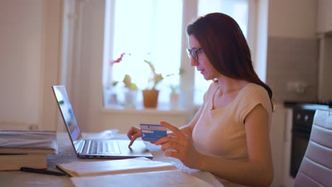 young woman pays for credit card shopping, uses laptop and enjoys it very much