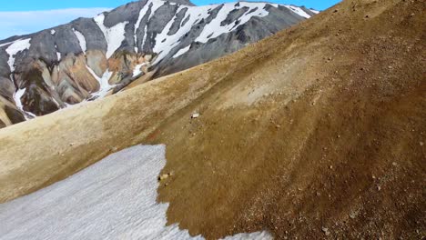 the aerial reveal of mountains covered with patches of snow and a wide valley with a glacier river flowing in a distance