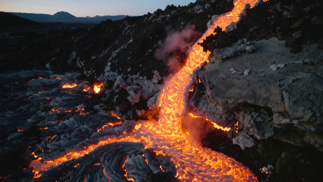 Flowing vent-fed molten lava cascade descending slope at lava field at dusk, feeding braided lobes