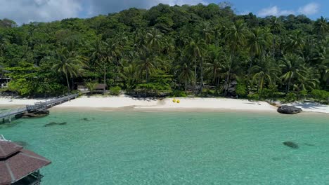 aerial, reverse, tilt up, drone shot away from a wooden pier, at a paradise beach, on a sunny day, in koh kood, thailand