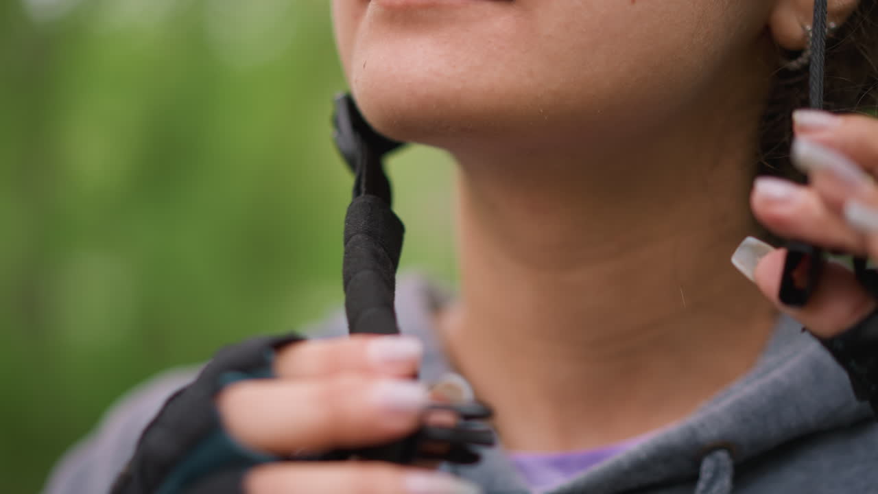 Asian Wellness Cyclist Checking Buckle At Chin, Adjusting Padding And Earrings Peeking Through Hair, Serene Expression Against Leafy Path, Small PreRide Comfort Check Before Setting Off